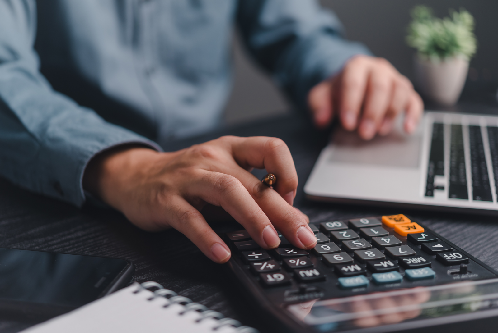 Someone working through figures on a calculator beside a laptop while planning a budget.