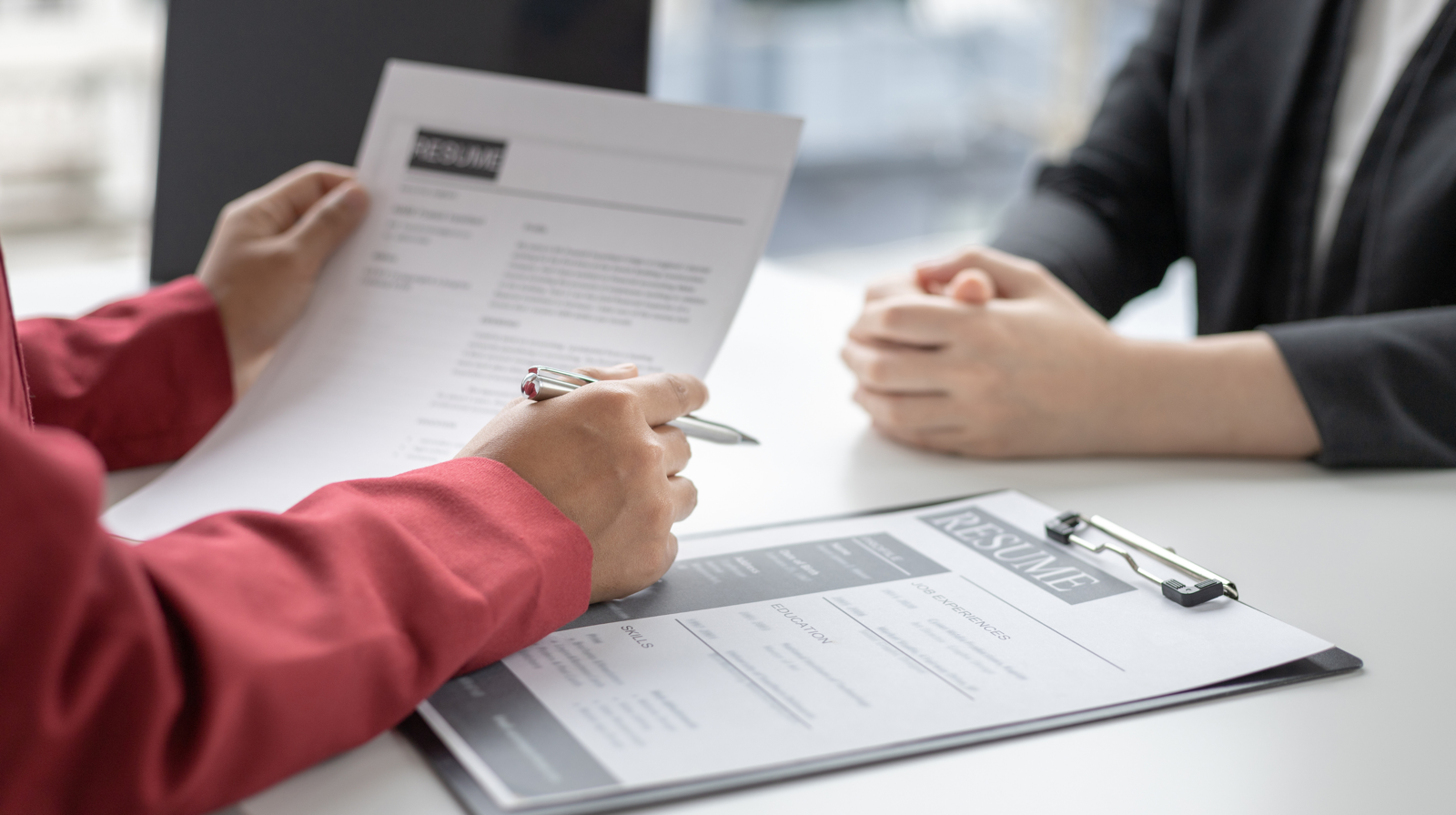 A hiring manager reviewing a candidate's resume across a desk during an interview.